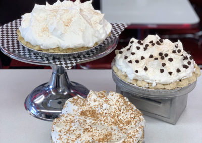 three cream pies with fun toppings displayed on a counter