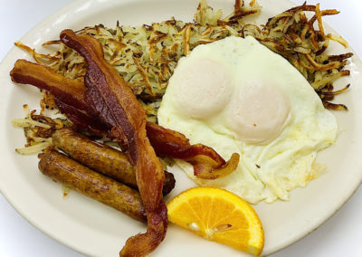a plate with sausage links, bacon, hash browns, fried eggs and an orange slice for garnish