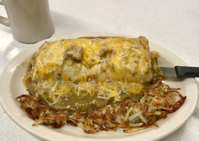 plate with hash brows and a breakfast burrito smothered in green chile sauce and cheese