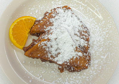 A plate with thick slices of french toast topped with powdered sugar and garnished with an orange slice