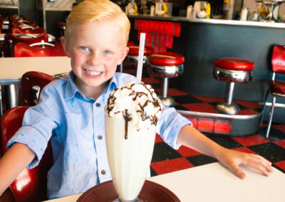 A smiling child at a diner table with a milkshake