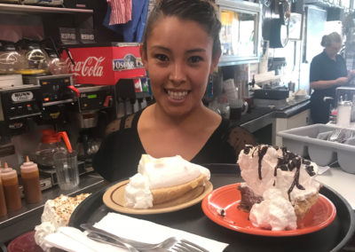 A smiling restaurant server carrying a tray with dessert plates