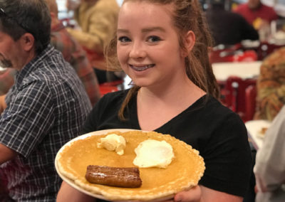 A smiling restaurant server carrying a plate of pancakes