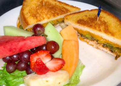 A plate with a grilled sandwich with diced green chile and cheese and a side of fresh fruit