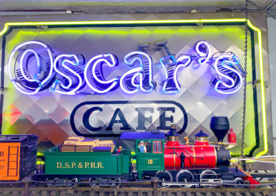 A toy train on tracks with a neon restaurant sign in the background